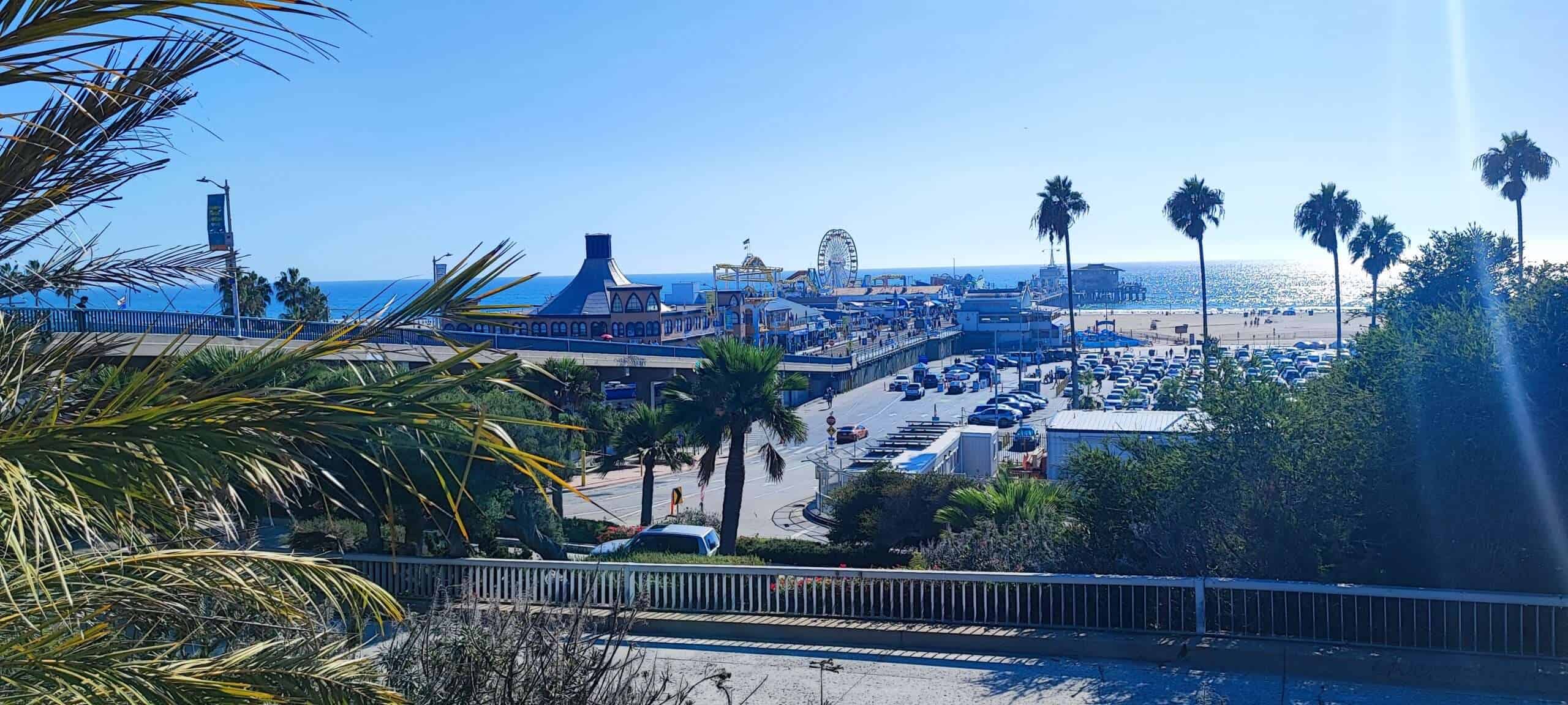 Blaue Himmel, Palmen und ein belebter Strand mit Freizeitpark und Parkhäusern in Santa Monica, Kalifornien, USA. Perfektes Sommerbild der kalifornischen Küste.