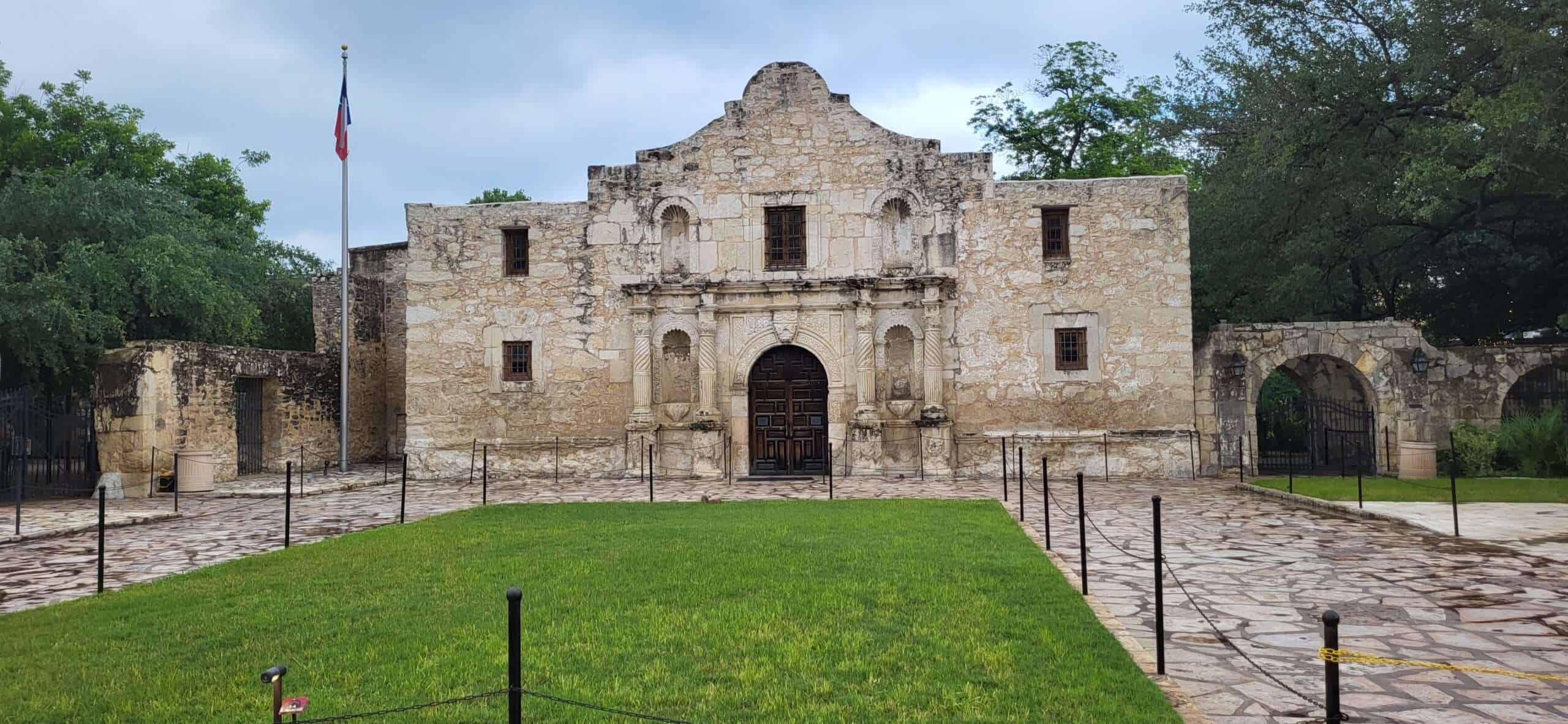 Historisches spanisches Missionsgebäude in San Antonio, Texas, mit Steinarchitektur, grünem Rasen und tropischem Himmel, symbolisiert die Altstadt und den kulturellen Wandel in den USA.