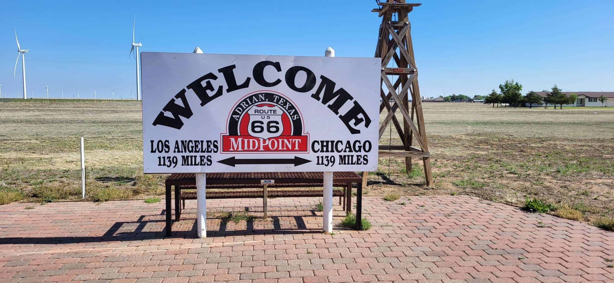 Midpoint 66 Route 66 Welcome Schild mit Windkraftanlagen im Hintergrund in Adrian, Texas, und Chikago, Illinois, USA, unterwegs auf der berühmten amerikanischen Route 66, Midpoint, Roadtrip, USA.