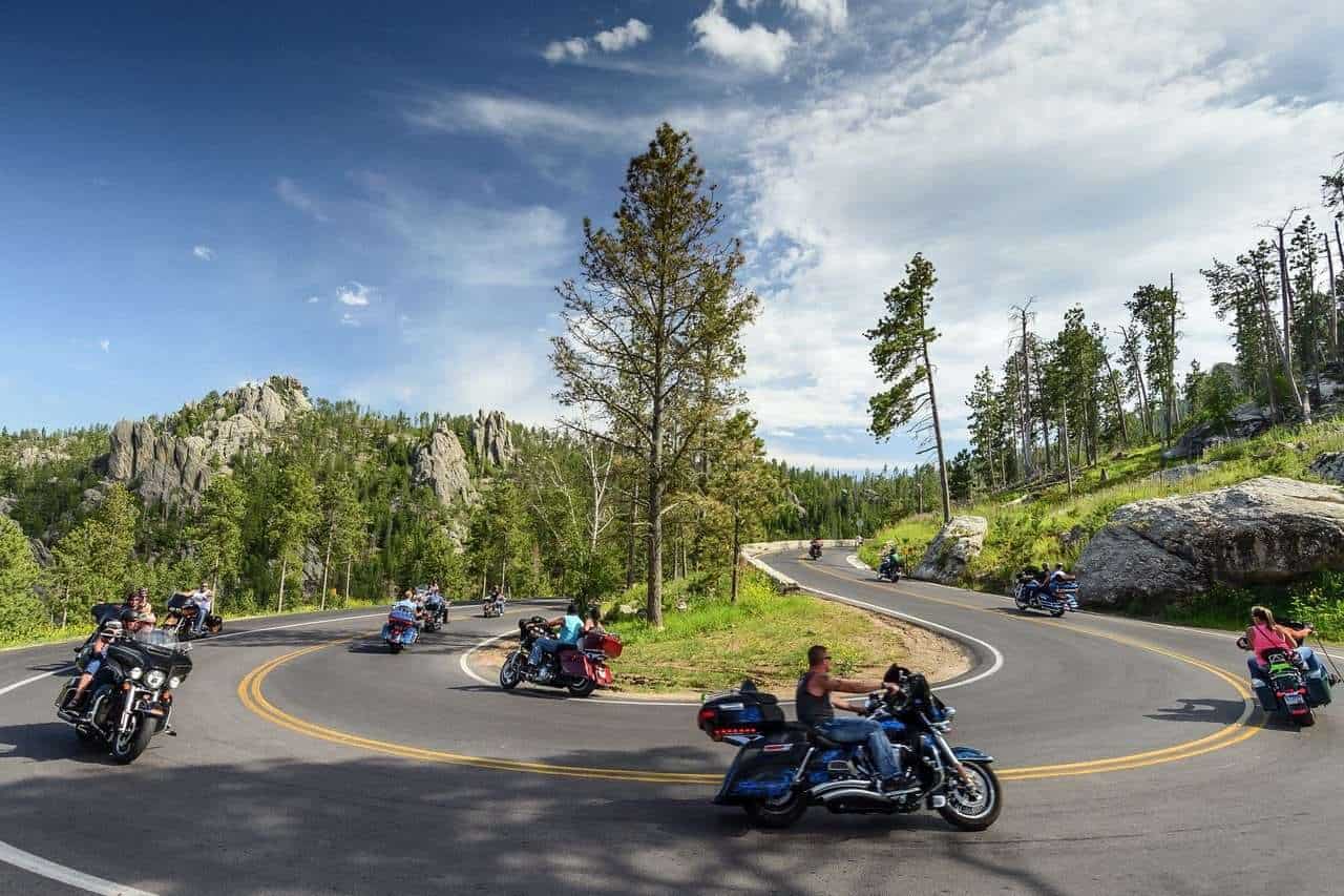 2. Atemberaubende Motorradtour auf kurviger Bergstraße im Nationalpark, umgeben von grünen Wäldern, Felsen und blauem Himmel in den USA.