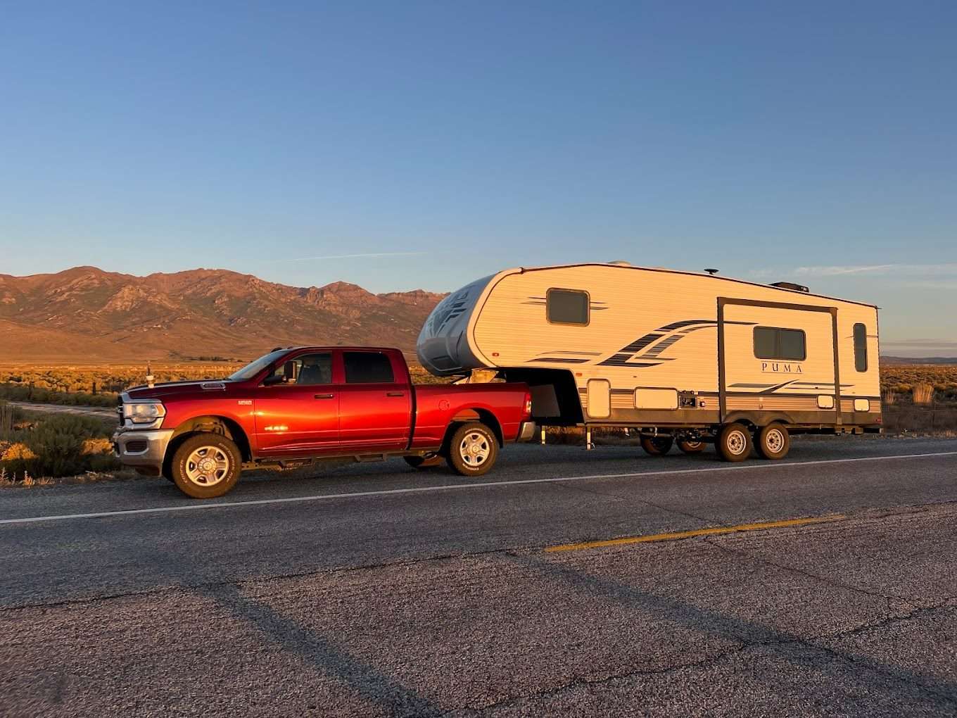 Hochwertige Reise mit Pickup-Truck und Wohnwagen in der amerikanischen Wüstenlandschaft bei Sonnenuntergang, Vorstellung des American Roadtrip-Feelings, offener Horizont und Berge im Hintergrund.
