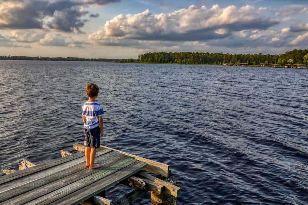 Photo by Mick Haupt boy in white t-shirt standing on wooden dock during daytime