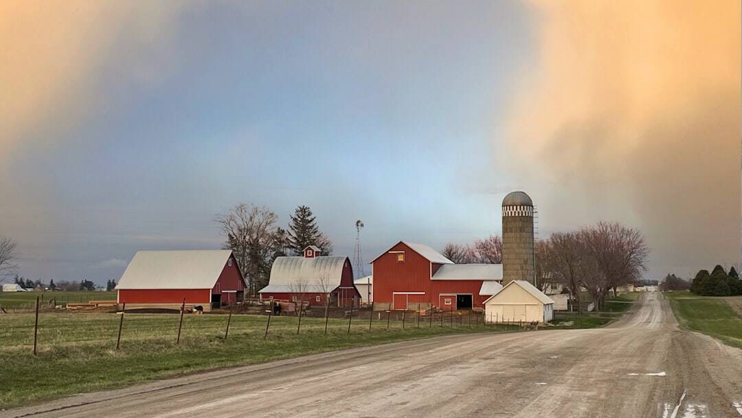 a dirt road leading to a farm with a barn and silo in the background