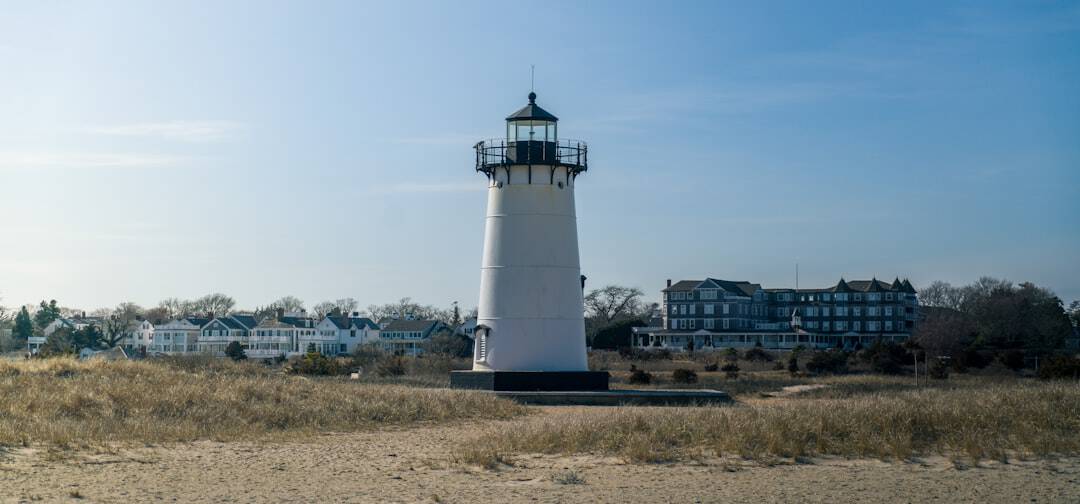 Photo by Mark Mialik a lighthouse on a beach with houses in the background